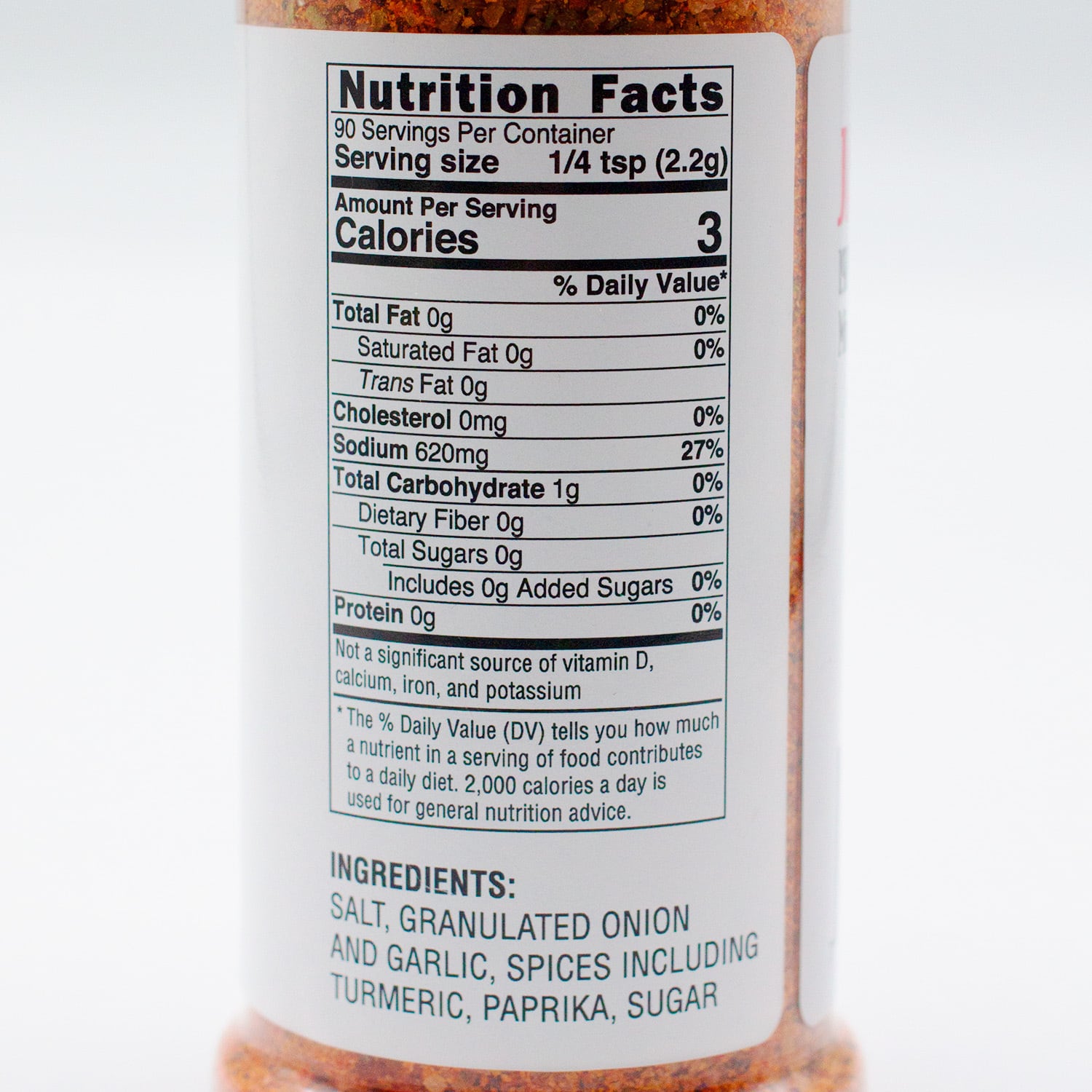 Nutrition facts label for a seasoning product. There are 90 servings per container, with a serving size of 1/4 teaspoon (2.2 grams). Each serving contains 3 calories. The product contains no fat, cholesterol, sugars, or protein. It has 620 milligrams of sodium, which is 27% of the daily value. The label notes that the product is not a significant source of vitamin D, calcium, iron, and potassium. Ingredients include salt, granulated onion and garlic, spices including turmeric, paprika, sugar, and others.
